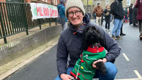 Alex Harris/BBC A man and a dog dressed in a Christmas cardigan