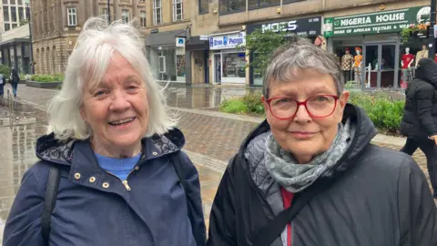 BBC/Grace Wood Two women in rain coats. The woman on the left has a white bob and the woman on the right has short grey hair