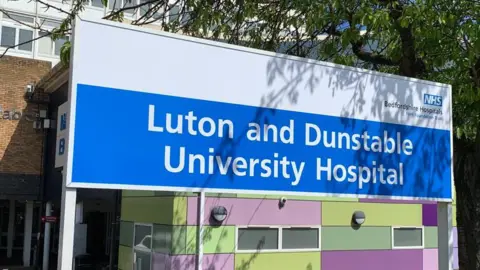 A sign of Luton and Dunstable Hospital with the building in the background.