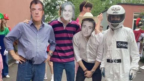Gordano School A group of four people wearing top gear cast masks. One is in a white driving suit with a white helmet on, dressed as the The Stig, then the mask of Jeremy Clarkson on the left, James May next to him and one dressed as Richard Hammond next to The Stig. They are wearing shirts. 