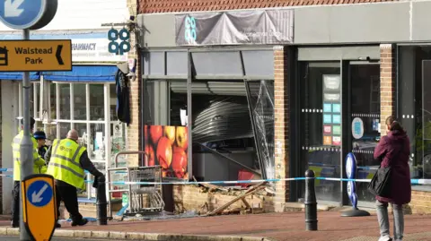 Supermarket workers and residents standing outside a Co-Op shop front which has been severely damaged.