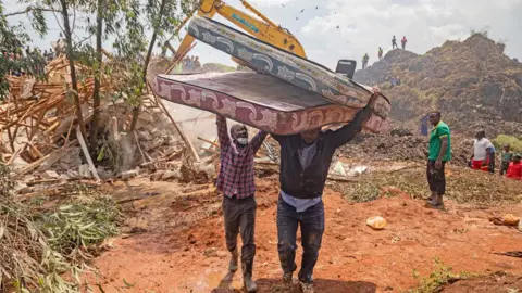 AFP Seorang pria mengangkat tangannya untuk membantu pria lain yang membawa kasur derek menjauh dari situs limbah Kiteezi setelah runtuhnya pada Agustus 2024 - Kampala, Uganda