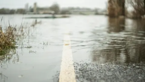 Getty Images A stock image of a partially flooded country road with a white line marking.