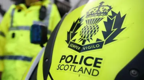 PA Media A 'POLICE SCOTLAND' name and emblem on a yellow vehicle background.