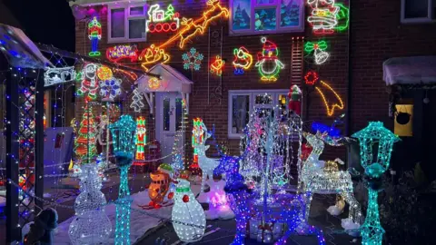 A house and front garden are completely covered in bright Christmas lights: glowing reindeer, snowmen, penguins, and Santa figures fill the space.