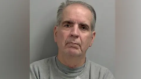 A police mugshot of Robert Alexander in a grey prison sweatshirt