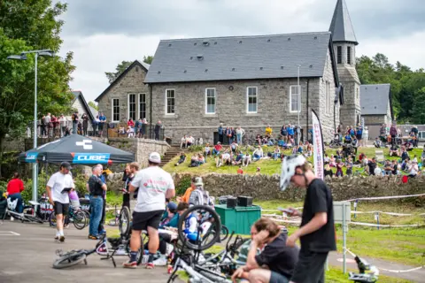 Pete Scullion A general scene of cyclists, spectators and a large, granite former school building in the background