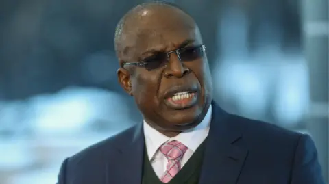 Bloomberg via Getty Images Timipre Sylva in a pink tie and navy pinstriped suit and dark glasses in 2020.