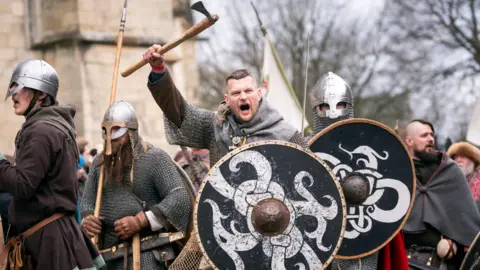 Danny Lawson/PA Wire Viking re-enactors during the Jorvik Viking Festival in York. A man in chain-mail with a black wooden shield shouts while holding an axe above his head