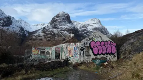 Harris Aslam family The cottage, pictured against the backdrop of Three Sisters mountains, has no roof and its white walls are covered in graffiti.