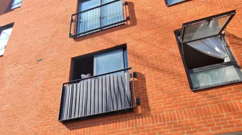 Red brick block of flats with an open window and balconies.