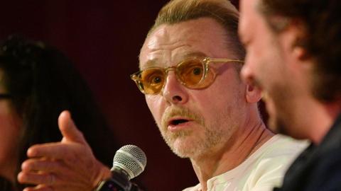 Simon Pegg gestures while speaking into a microphone onstage with Edgar Wright during a 20th anniversary screening and Q&A of Shaun of the Dead at Glastonbury Festival in June 2024