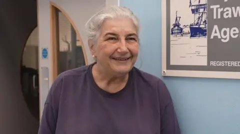 Alison Pessell smiles at the camera wearing a purple tshirt