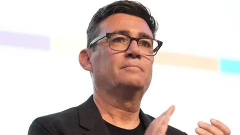 Andy Burnham claps while wearing a black suit