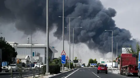 Getty Images Motorists drive past a plume of smoke rising from a reported Iranian strike in the industrial district of Doha on March 1, 2026. 