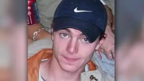 A headshot image of Luke Durbin. A young man wearing a navy Nike baseball cap. He is smiling and looking directly into the camera. 