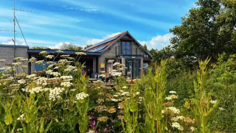 Ellen Leach A wooden chalet behind a field of wildflowers
