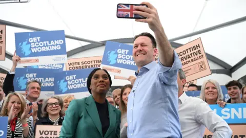 PA Media Russell Findlay takes a selfie with Kemi Badenoch at a campaign event. There are activists behind them holding posters.