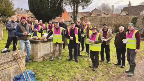 National Churches Trust Several people are stood in hi-vis jackets holding food and drink in a churchyard.