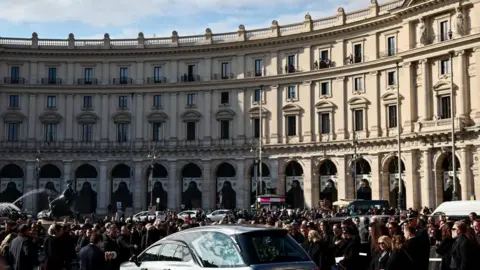 REUTERS/Yara Nardi A large crowd gathers in a city square as the hearse carrying the coffin arrives for the funeral ceremony.