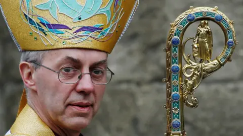 Justin Welby. He has short grey hair and wears glasses. He has an ornate hat and is carrying a crozier.