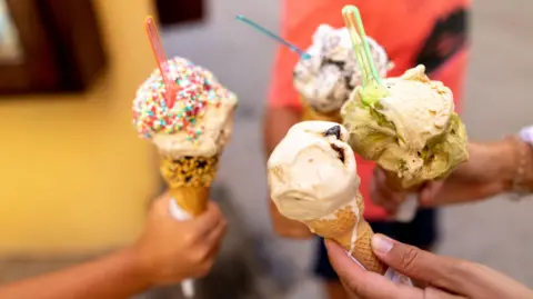 Getty Images A generic shot of hands holding different flavour ice creams in cones. 