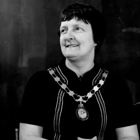 Kenneth Black Mary sitting at a desk wearing a dark top and medal. She has short dark hair.
