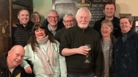 Handout Members of the Old Horn Community Pub Society committee. There are 10 people in the photo, who are all smiling.