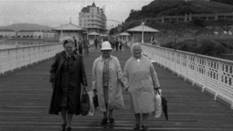 Three women holding bags walking along a pier.