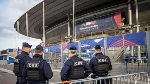 Four French police officers stand outside the Stade de France stadium wearing jackets with CRS on them before training sessions of the teams of France and Israel