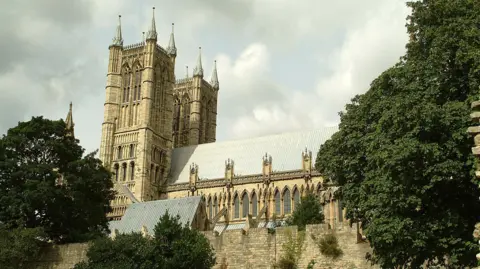 BBC The building captured from a side angle (in landscape view). The two ornate towers are to the left of the picture and the rest of the building with its grey roof stretches out behind the towers. The building is surrounded by walls.