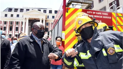 Reuters South African President Cyril Ramaphosa bumps elbows with a firefighter as he inspects damages after a fire broke out at the Parliament building in Cape Town, South Africa, January 2, 2022