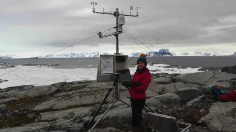 British Antarctic Survey Scientist working in front of a large aerial with snowy mountains in the background