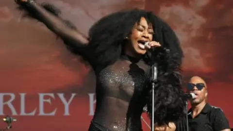 Beverley Knight performing at Godiva Festival 2024. Her right arm is outstretched and her left arm is holding a microphone.