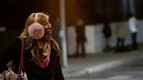 Reuters A woman wearing a protective face mask and earmuffs crosses the street during the outbreak of the coronavirus disease) in Beverly Hills, California, US, November 20, 2020