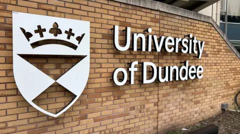 BBC Logo Universitas Dundee dalam huruf putih di dinding bata