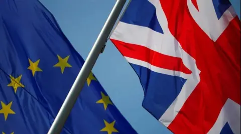 An EU flag and a UK flag with a blue sky behind.