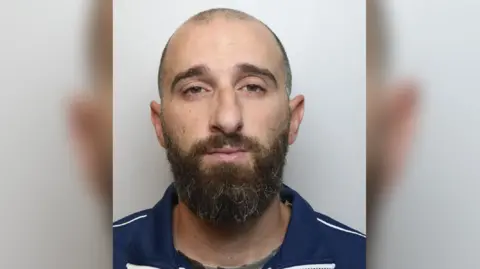 National Crime Agency Police handout of Sorrenti - balding with mostly shaved head, but bushier brown beard, wearing a dark blue top.