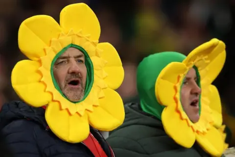 Getty Images Two men in daffodil hats singing.