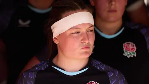 Sophie McQueen, wearing an England shirt and a white headband, waits in the tunnel before a match.