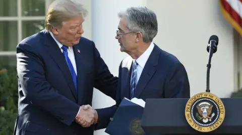 Getty Images US President Donald Trump, wearing a dark blue suit, white shirt and electric blue tie, shakes hands with his nominee for chairman of the Federal Reserve, Jerome Powell. He wears a dark blue suit, a white shirt and a blue and silver tie.
