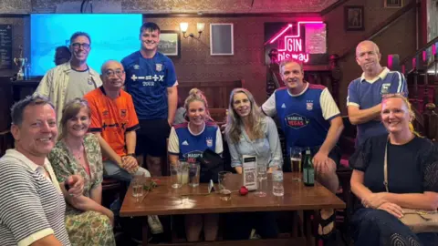 Kate Czarnecki Ten football fans - several wearing Ipswich Town replica shirts - crowded around a table in a bar
