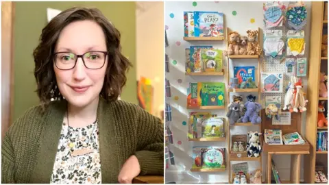  A selfie of a woman, smiling, with shoulder-length brown hair, dark glasses, a green cardigan and a floral green and white top, sat inside a room with walls painted green; A display of soft toys, books and bibs in a gift shop