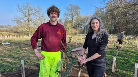 Swindon Borough Council A smiling man and woman stand in a field of saplings. The woman rests her hands on a spade.