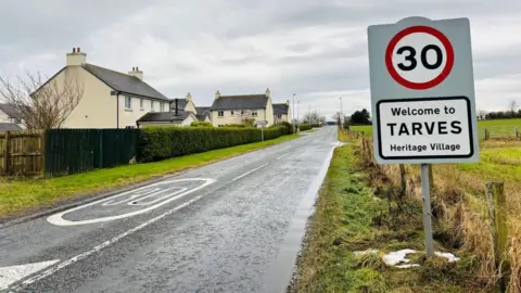 A picture of the road leading into Tarves, with a 30mph sign next to a field, and housing on the other side.