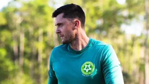 Gavin Carlin, entrenador del Good Lad Soccer / O'Neill's Foyle Cup, tiene el pelo corto y castaño, lleva una camiseta verde y mira hacia un lado.