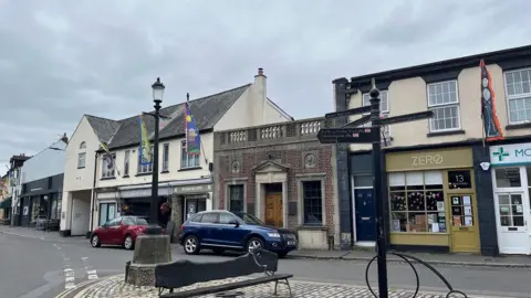 A bench and signpost on the square in Moretonhampstead with flags up on a building to the left.