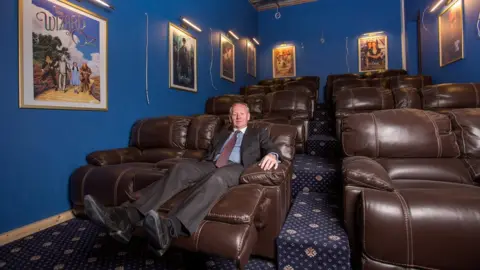 SWNS Graham Wildin sat in his cinema