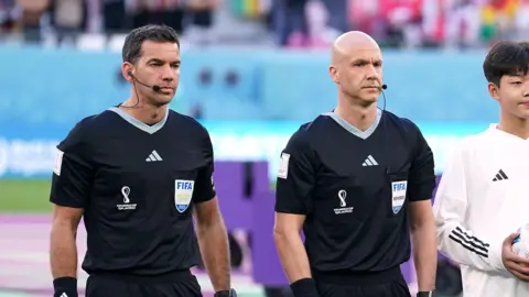 PA Adam Nunn stands next to referee Anthony Taylor in official Fifa referee black uniforms as they line up before a game.
