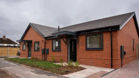 A red brick newly built bungalow with a black frin door and dark grey windows